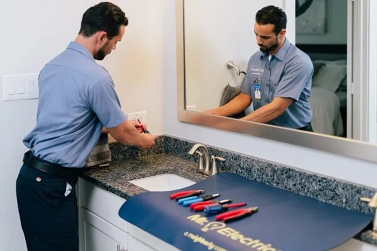 A Mr. Electric Electrician at a Bathroom Vanity Working on an Outlet with a Mr. Electric Mat with Tools on it on the Counter