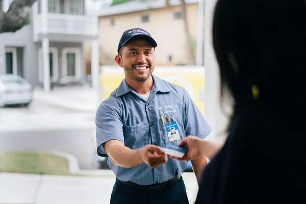 A Woman in Shadow Pictured from Behind Take a Business Card from a Smiling Mr. Electric Electrician Standing Outside Her Door